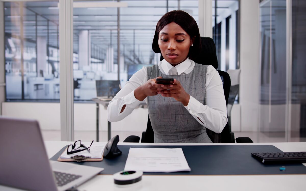 Business professional using smartphone at desk with computer, representing digital document management and OCR scanning technology.