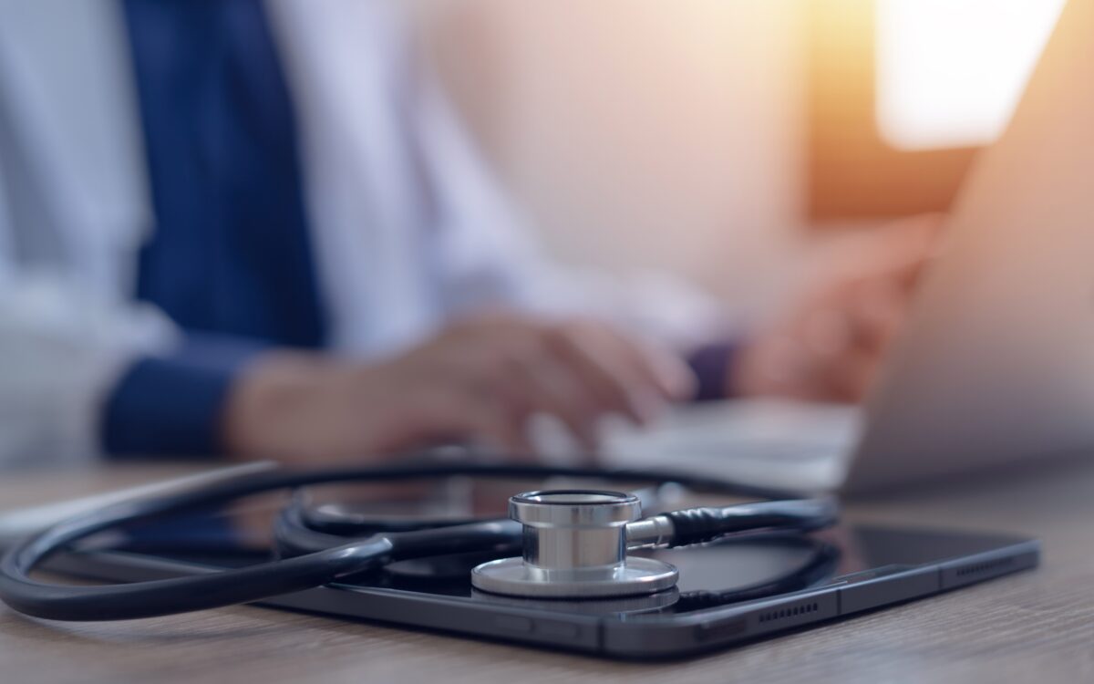 Stethoscope on tablet with doctor using laptop in background, symbolizing digitized medical records and electronic health record management.