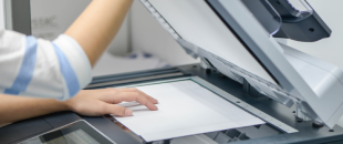 Person scanning paper documents on a flatbed scanner, illustrating the process and costs of document scanning and digitization services.
