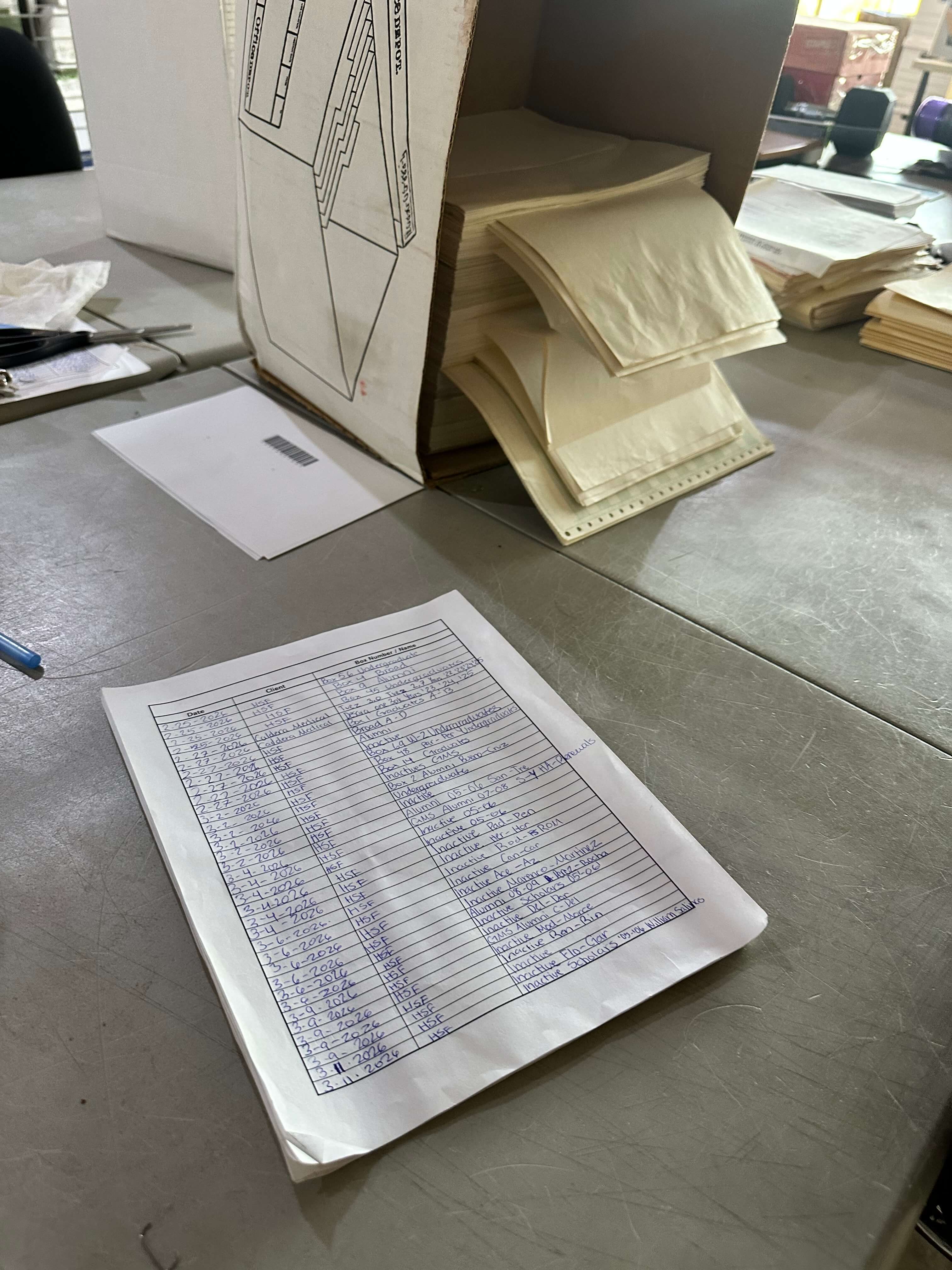 A handwritten production log sheet tracking client name, box number, and date next to document boxes in a scanning facility