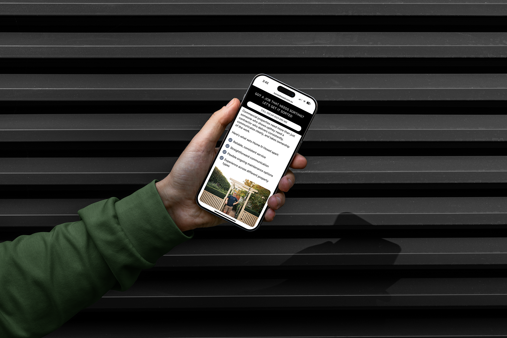 Hand holding a mobile phone displaying the Home N Hosed website outdoors