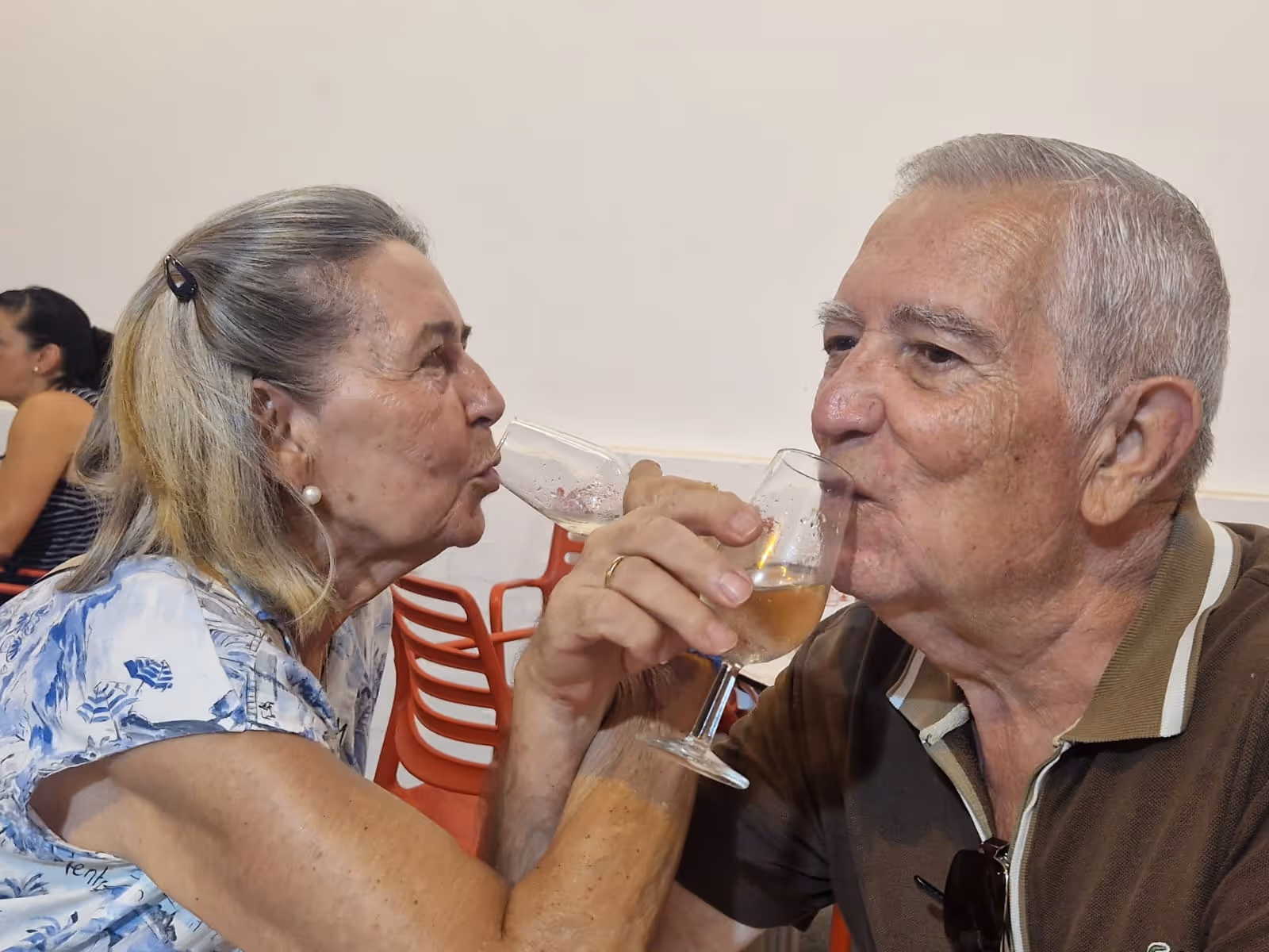 Pareja mayor brindando con copas de vino rosado mientras están sentados.
