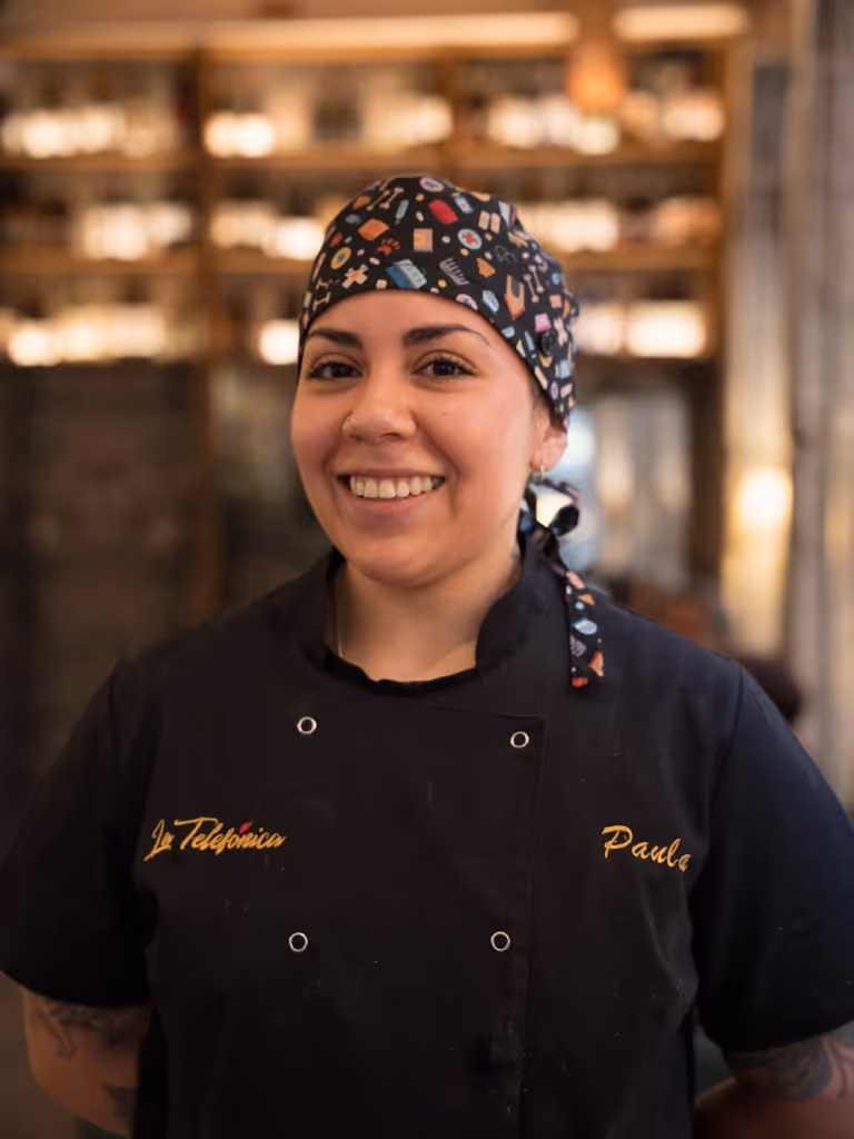 Mujer sonriente con gorro y uniforme de chef negro en un restaurante.