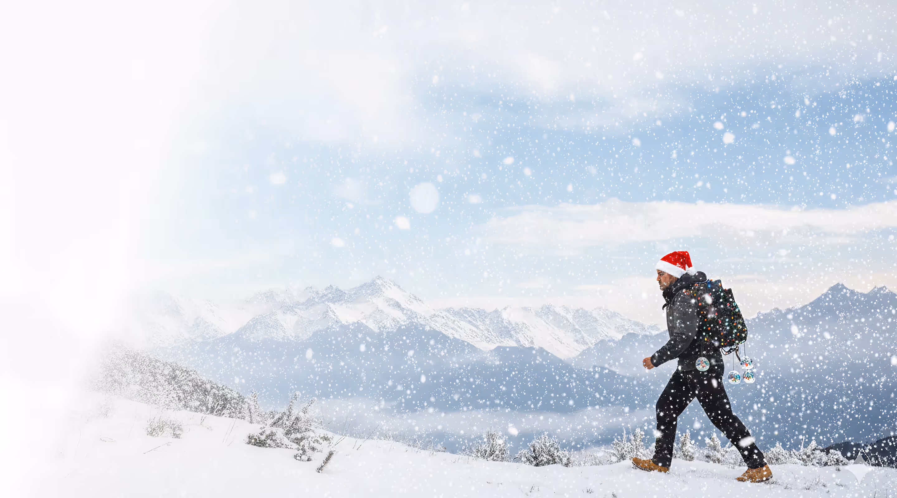 Man wearing a Santa hat and backpack walking through snowy mountains during snowfall.