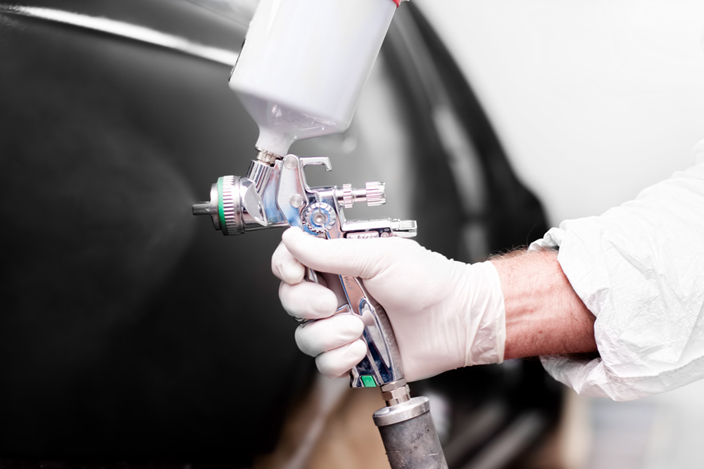 Worker using paint spray gun for painting a car