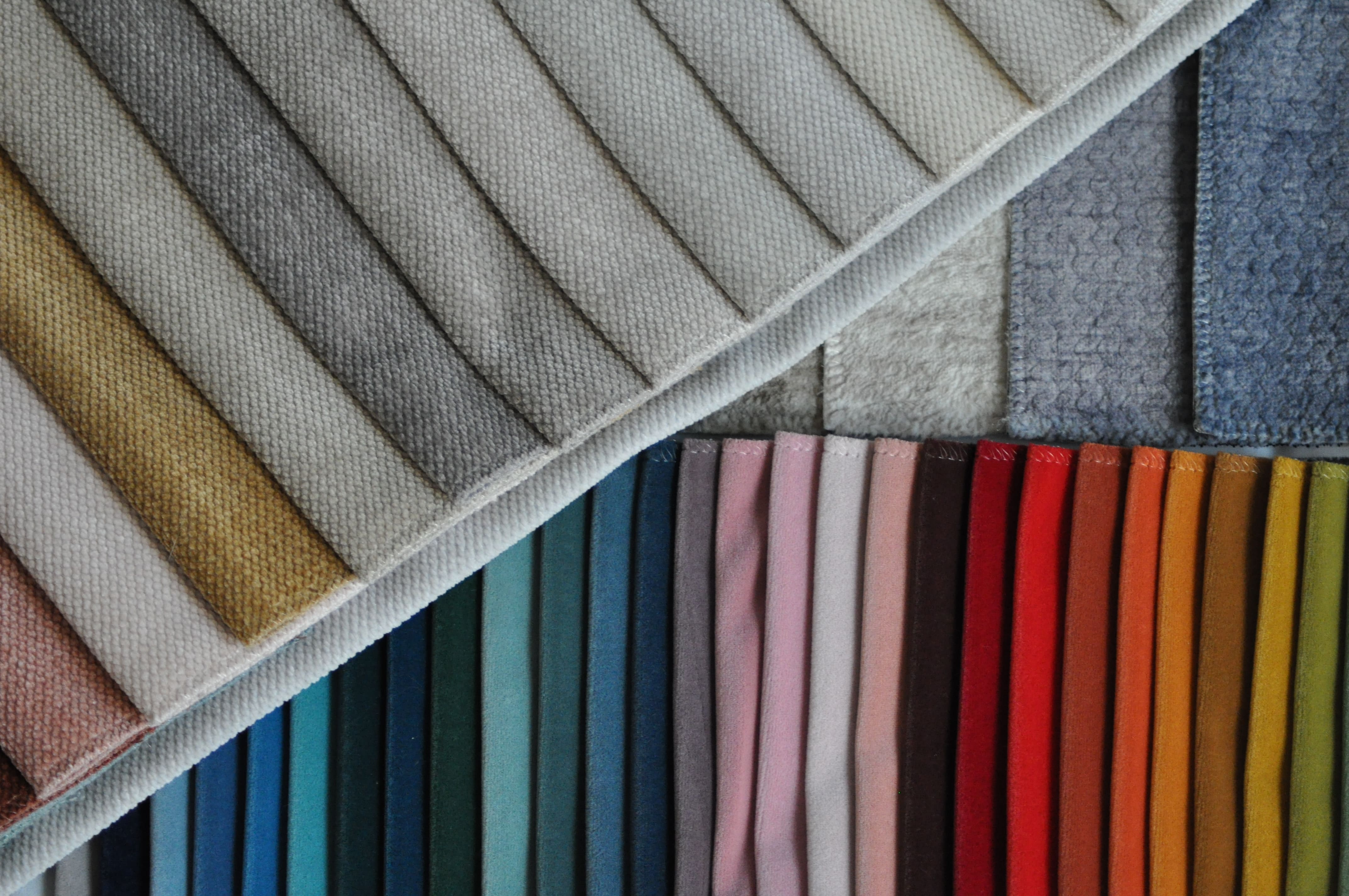 A gray dining room with a round black table, white chairs, and a geometric gold chandelier. To the left is a fireplace with stacked logs, and a doorway leads to another room.