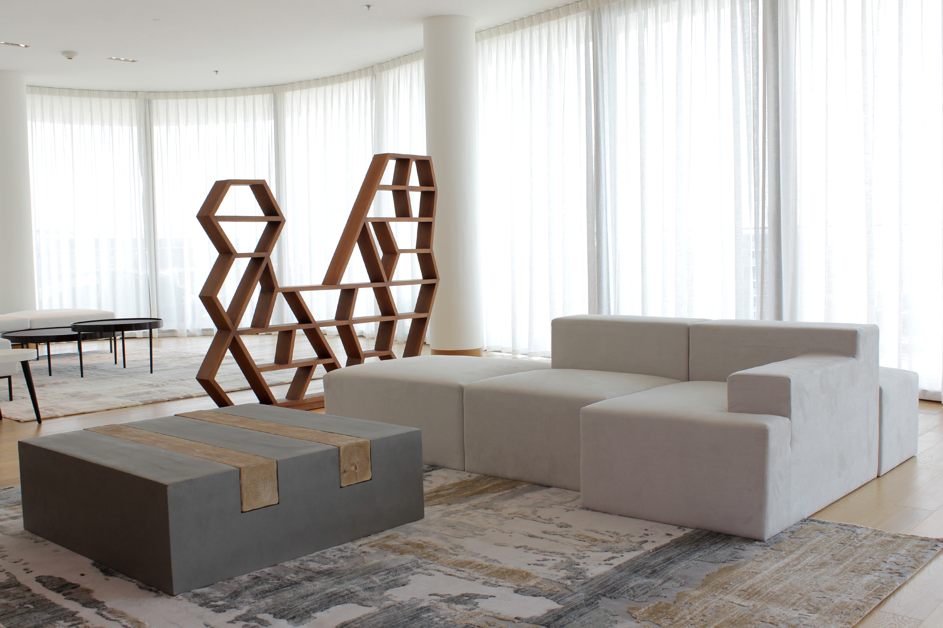 A bright living room features a light gray armchair with yellow and striped pillows, a light-colored sofa, and a wall adorned with a cluster of round, gold-framed mirrors.