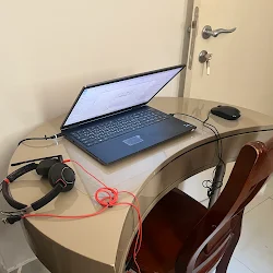 A luxurious bedroom showcases a white upholstered bed, gold chandelier, fuzzy white stools, and a black and white striped rug with a city view.