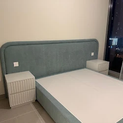 A luxurious bedroom showcases a white upholstered bed, gold chandelier, fuzzy white stools, and a black and white striped rug with a city view.
