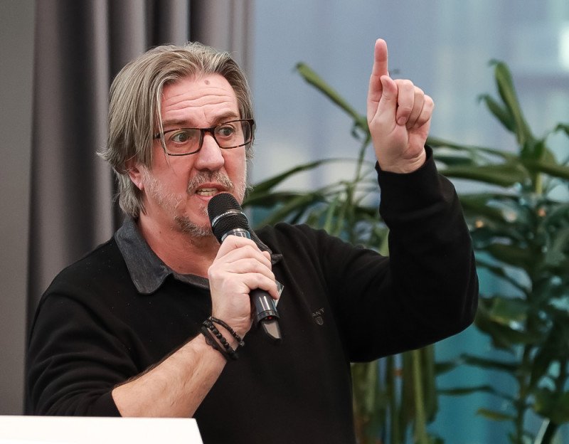 Halász Gyula kreatív igazgató mikrofonnal, felemelt kézzel előad
