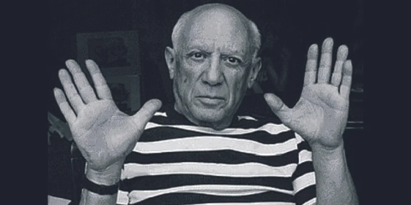 Pablo Picasso fekete-fehér portréja csíkos pólóban, két feltartott tenyérrel