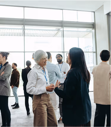 A woman in a white shirt and blue lanyard is talking to a woman in a black jacket.