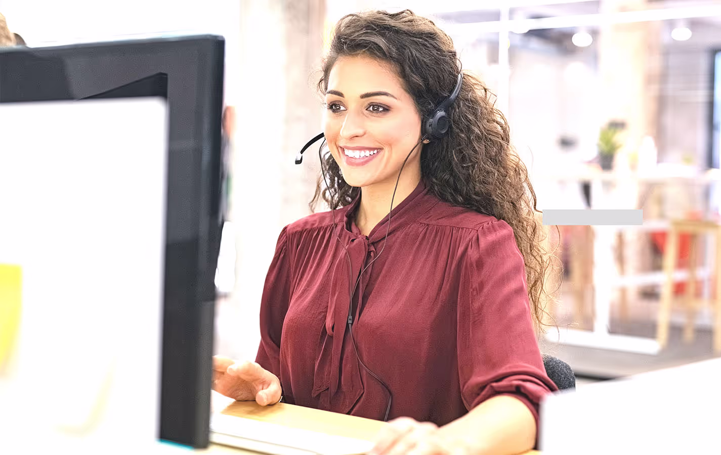 Smiling Account Executive on computer with headset at desk coordinating executive relocation services for VIP transferee.