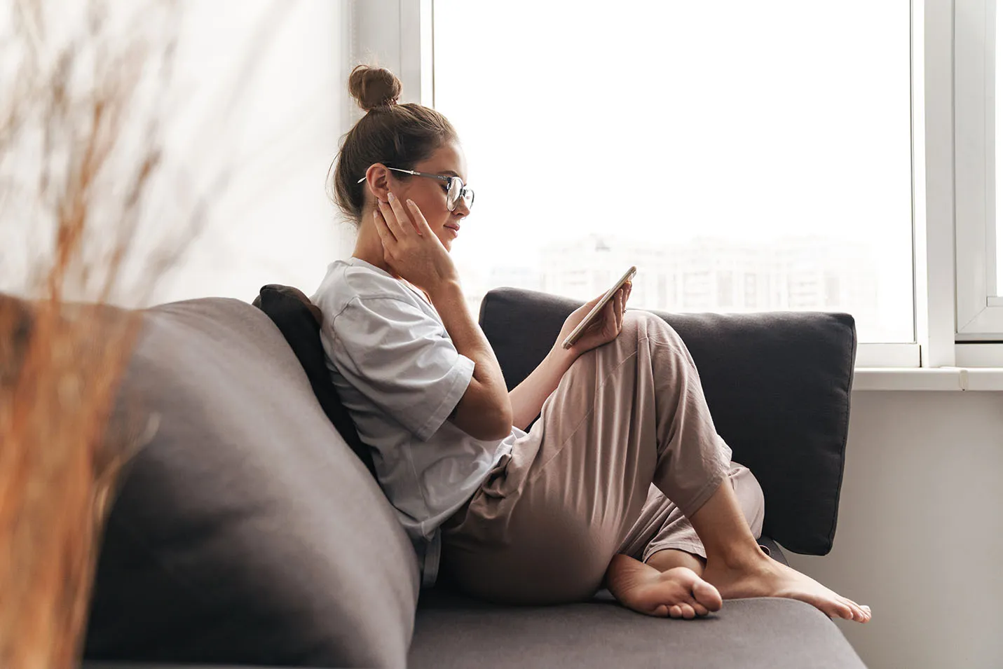 Female transferee emailing Account Executive from mobile device while sitting on gray couch.