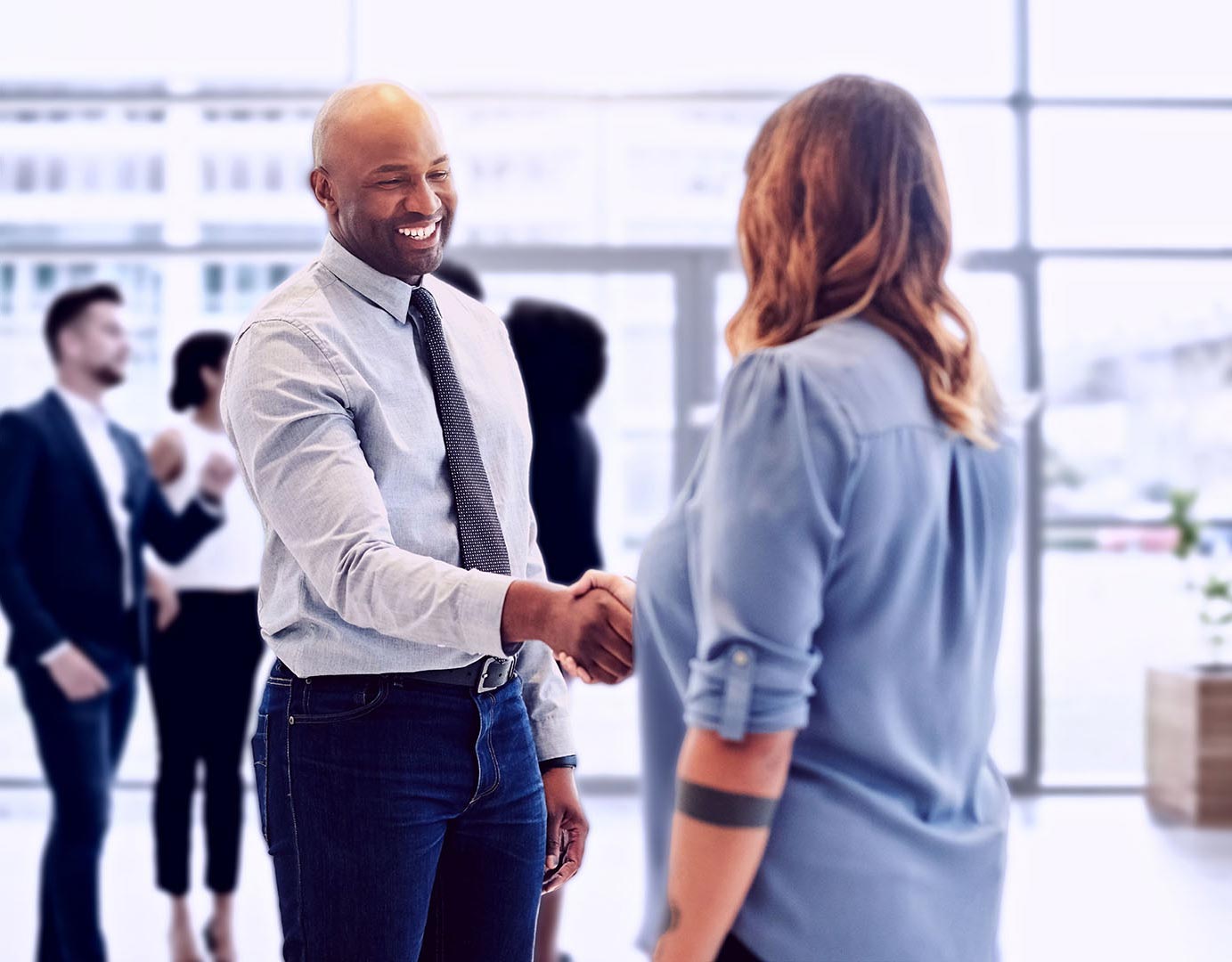 Male hiring manager meeting a female potential employee in a lobby, smiling and shaking hands.