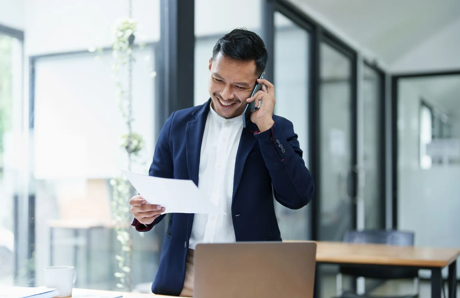 man on phone smiling, looking at a piece of paper while holding it in his hand