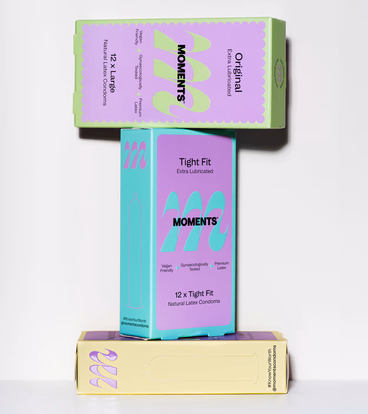 Three colorful MOMENTS condom boxes stacked, labeled Original Large, Tight Fit, and a yellow box at the bottom.