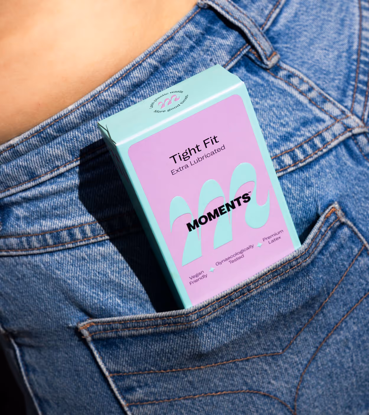 Blue and pink MOMENTS condom box labeled Tight Fit Extra Lubricated tucked in the front pocket of blue denim jeans.