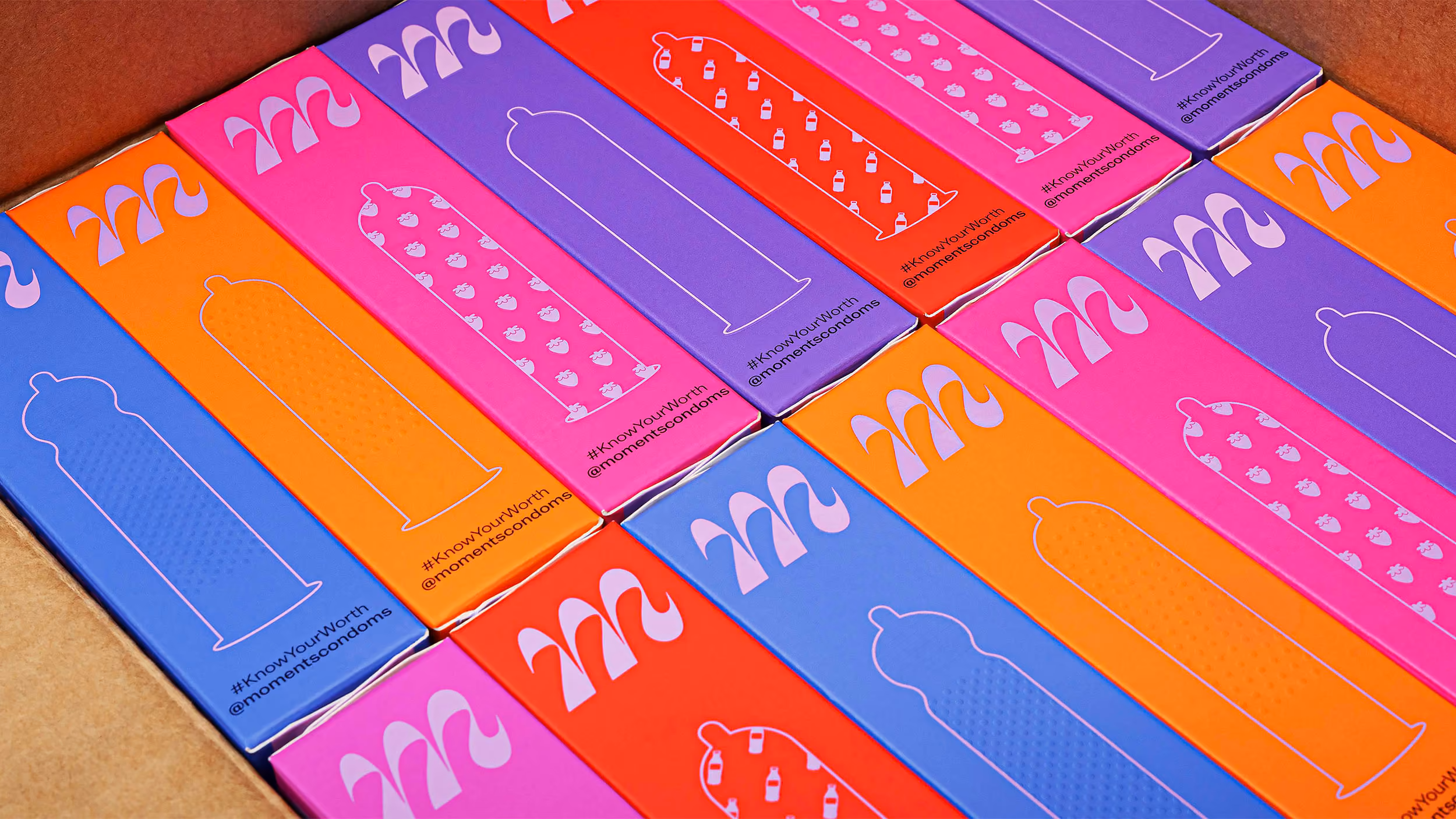 Colorful boxes of condoms with various patterns and #KnowYourWorth @momentscondoms branding arranged in a cardboard box.
