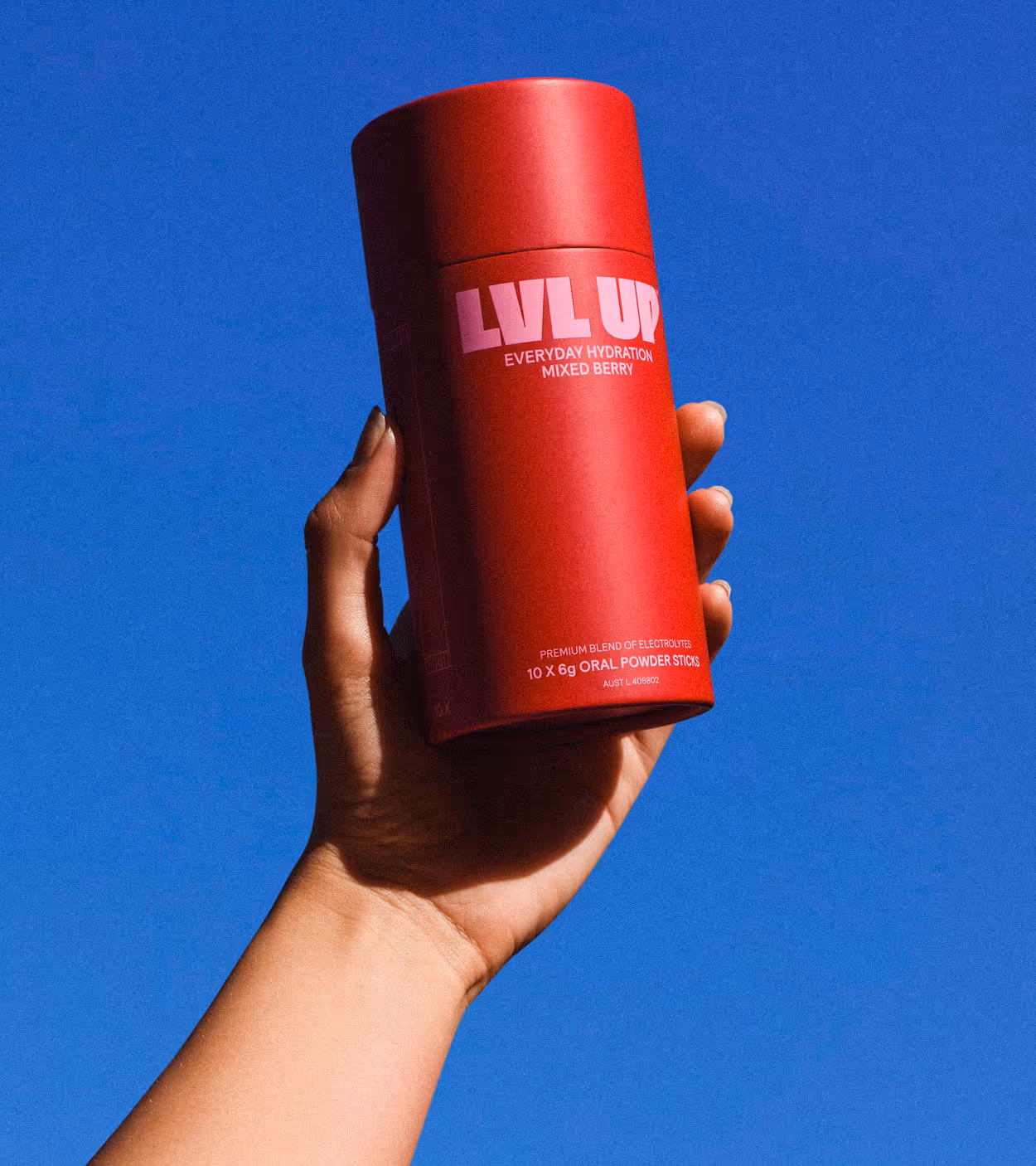 Hand holding a red cylindrical container labeled 'LVL UP Everyday Hydration Mixed Berry' against a clear blue sky.