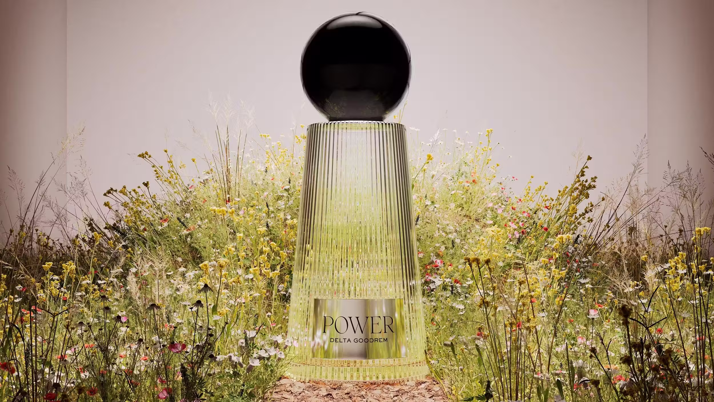A bottle of POWER by Delta Goodrem perfume with a black spherical cap, surrounded by wildflowers on a bed of dried leaves.