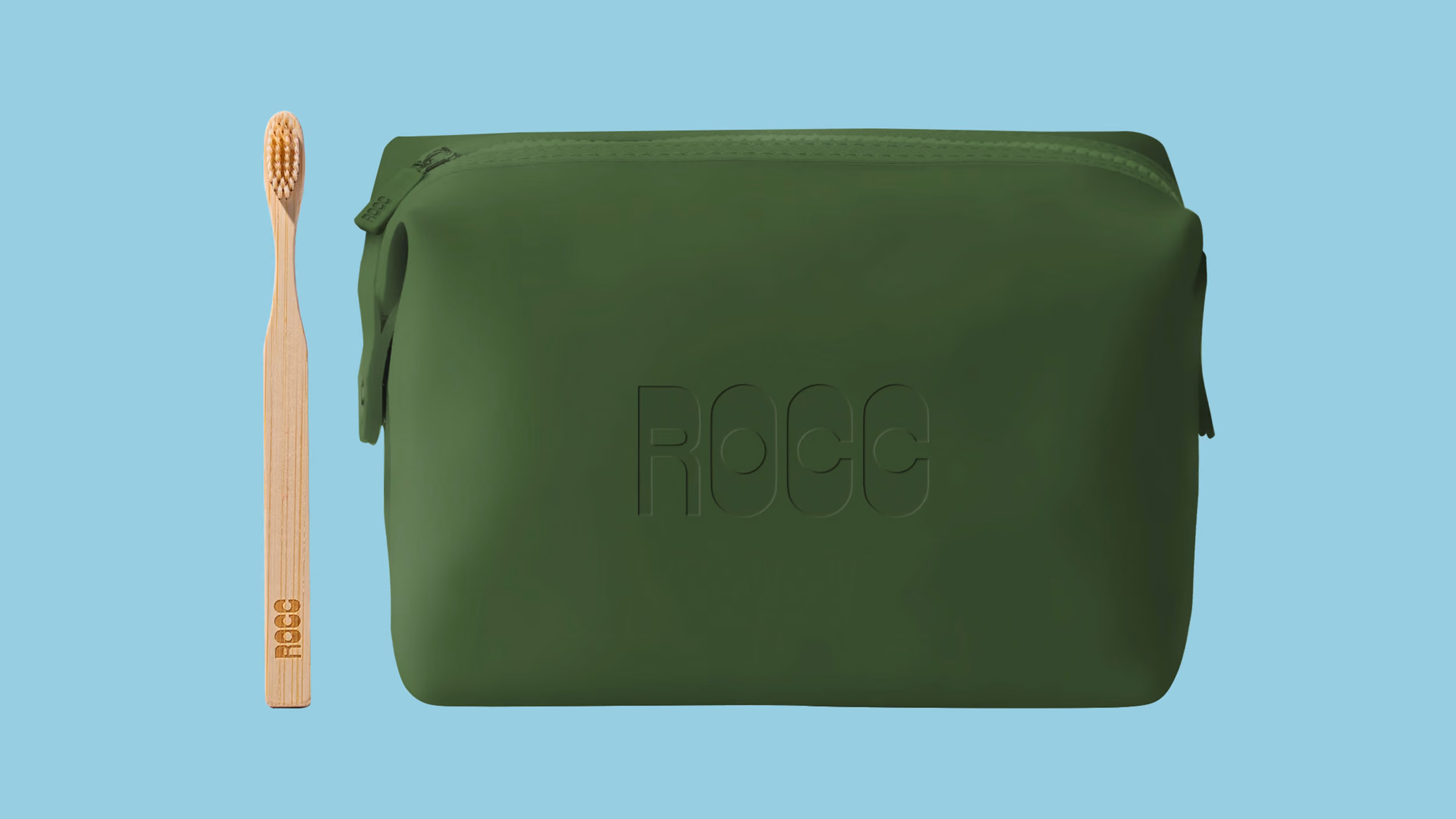 Green ROCC pouch with zipper beside a bamboo toothbrush with ROCC engraving on a light blue background.