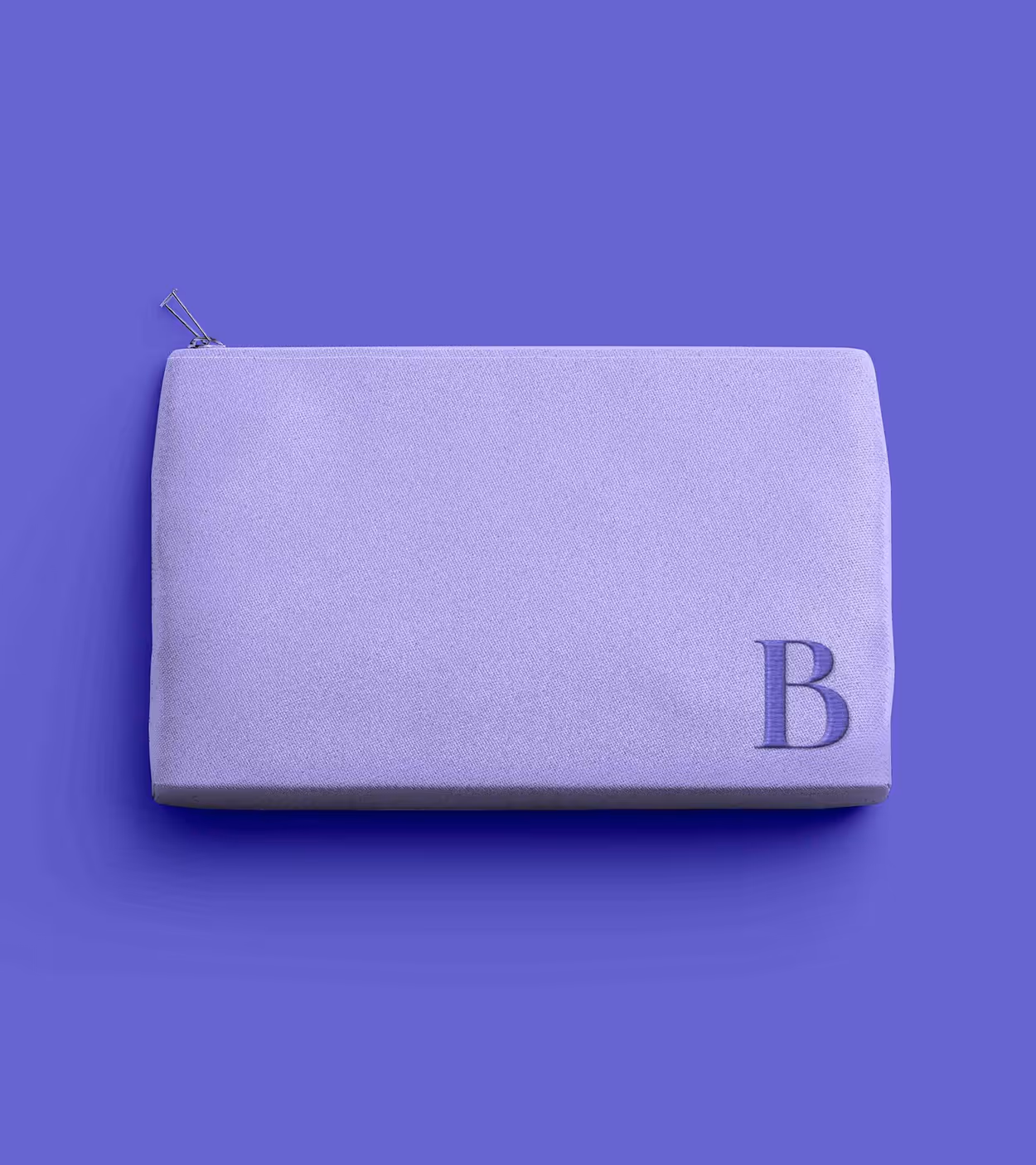 Rectangular lavender-colored fabric pouch with a zipper and a letter B embossed in the bottom right corner.