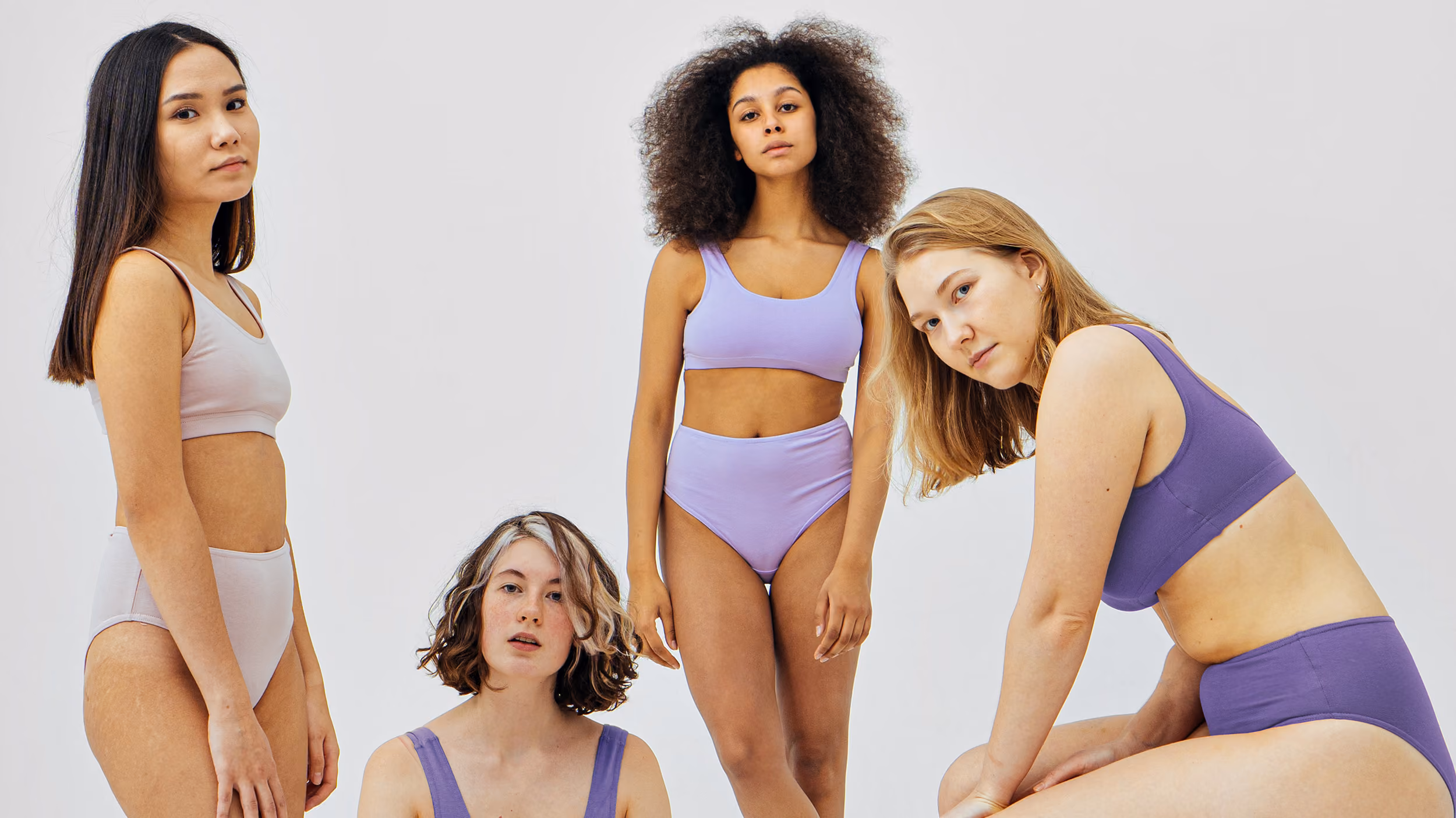 Four diverse women in pastel-colored underwear posing against a plain light background.