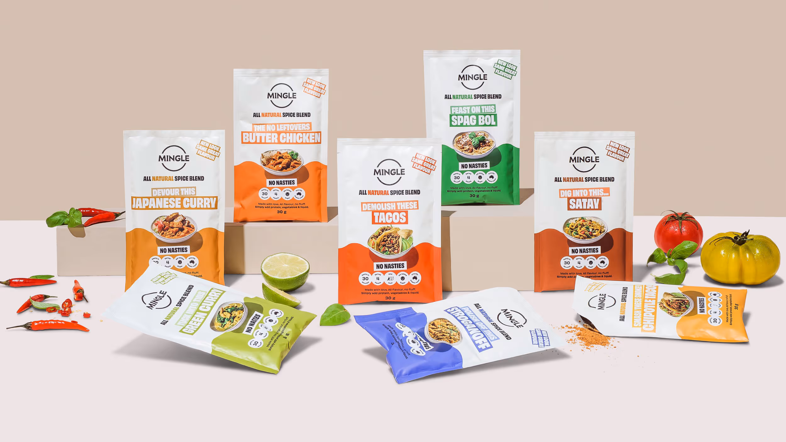 Seven colorful Mingle all natural spice blend sachets labeled for Japanese curry, butter chicken, tacos, spaghetti bolognese, satay, green curry, stroganoff, and chipotle fajitas, arranged with fresh ingredients on beige and pale backgrounds.