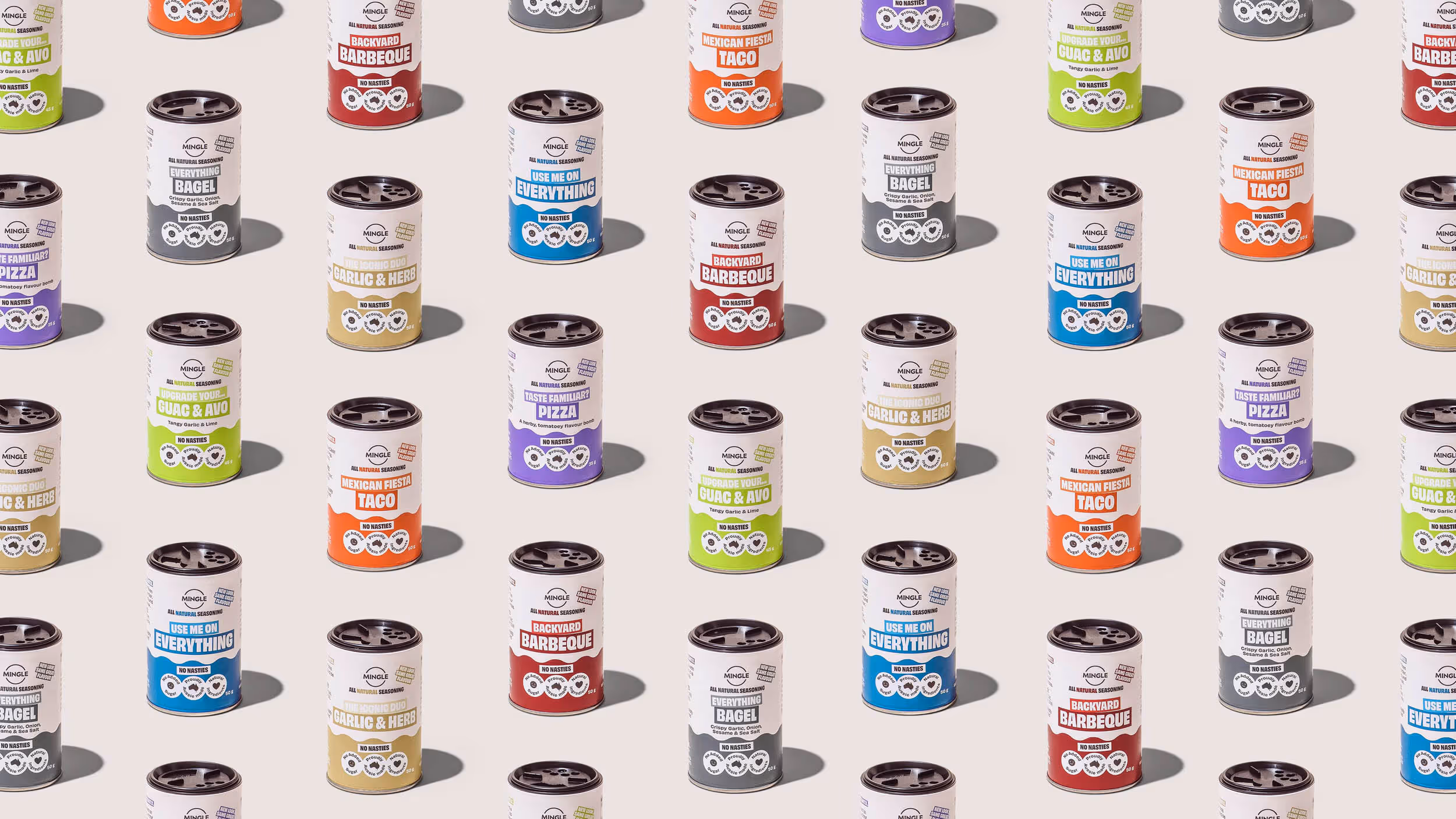 Multiple cans of Mingle all natural seasoning in various flavors like Backyard Barbeque, Mexican Fiesta Taco, Everything Bagel, Upgrade Your Guac & Avo, Taste Familiar? Pizza, and The Iconic Duo Garlic & Herb arranged on a light background.