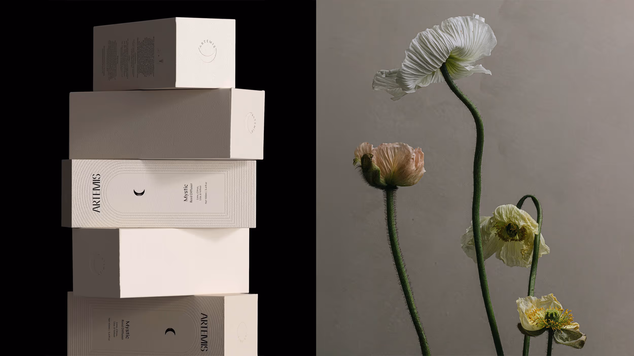 Stack of Artemis Mystic Reed Diffuser boxes beside white and pale pink flowers with long green stems.