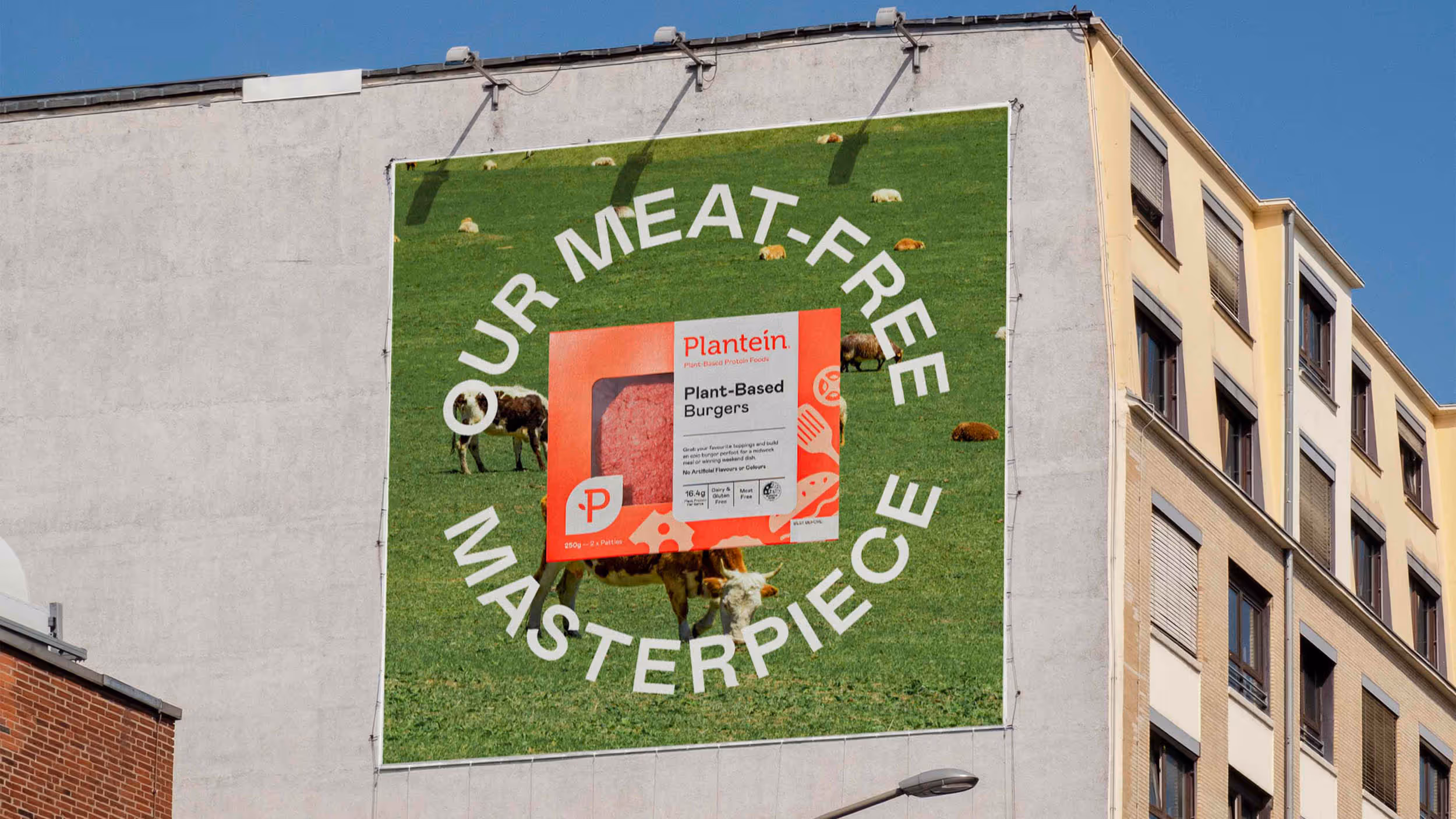 Large billboard on a building wall showing Plantein plant-based burger packaging with cows grazing on green grass background and text 'Our Meat-Free Masterpiece'.