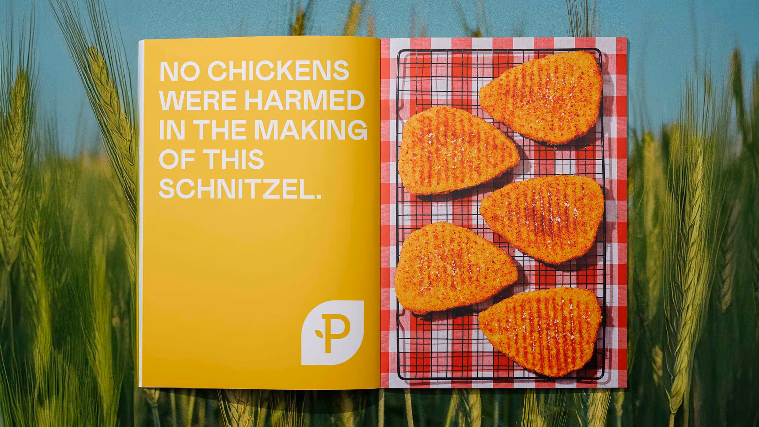Open book with yellow page reading 'No chickens were harmed in the making of this schnitzel' and a page showing five grilled plant-based schnitzels on a red and white checkered cloth.