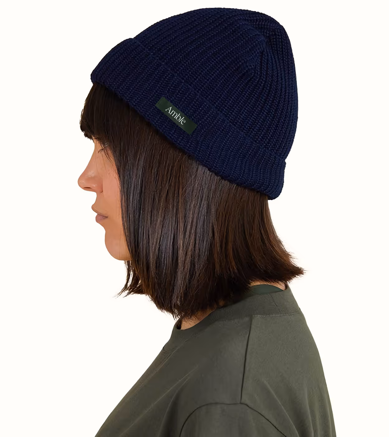 Side profile of a woman wearing a navy blue knit beanie and an olive green top.