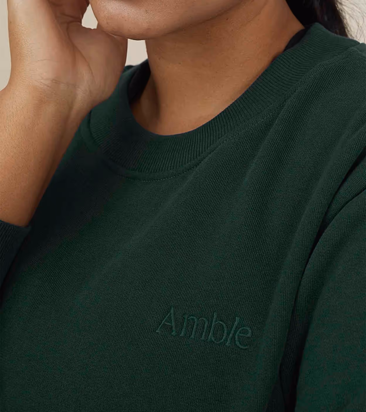 Close-up of a person wearing a dark green sweater with the word 'Amble' embroidered on the chest.
