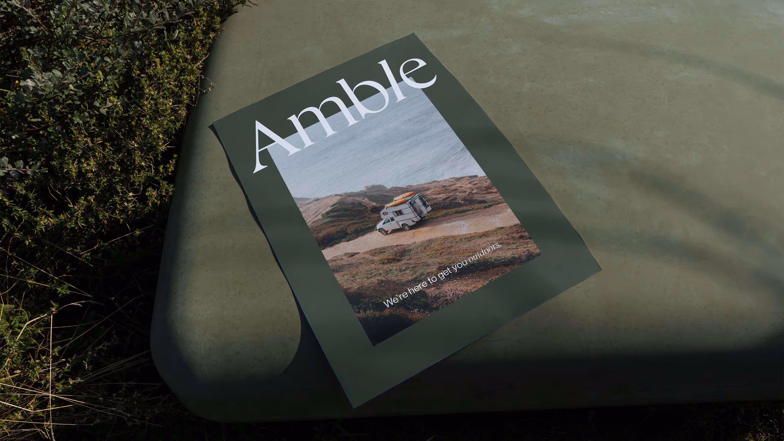 A green outdoor table with a poster of a camper van driving along a coastal dirt road and the text 'Amble' and 'We're here to get you outdoors.'