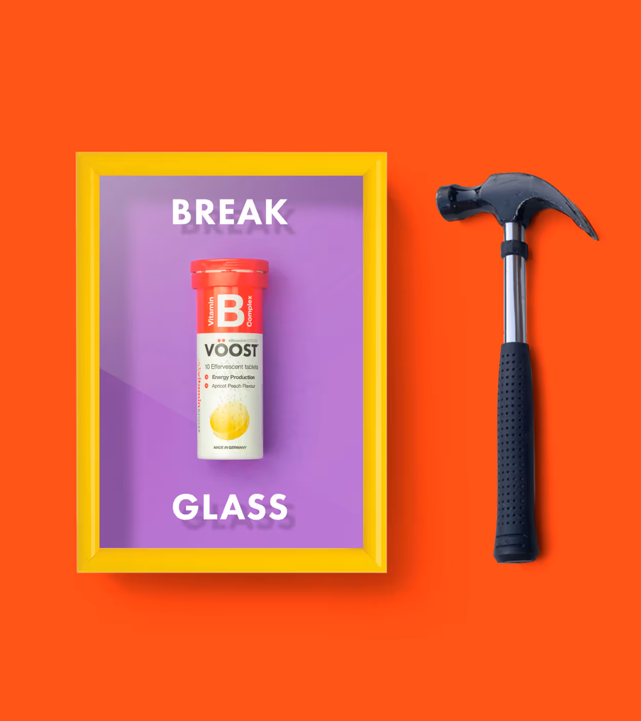 Yellow-framed glass panel with a VOOST vitamin B effervescent tablets tube inside, next to a hammer on a red background.
