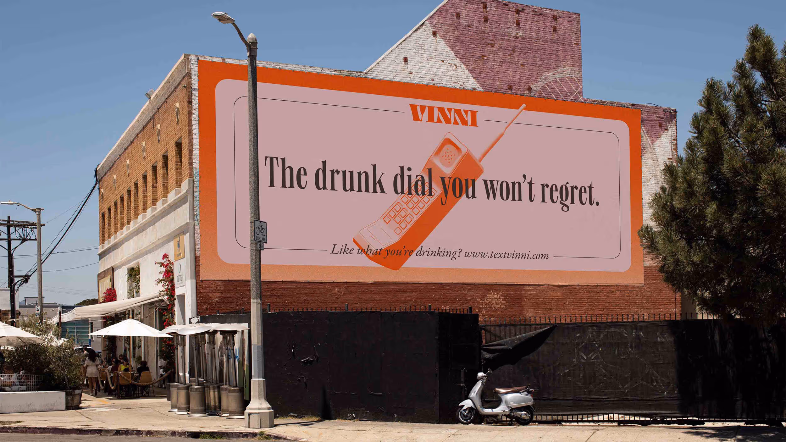 Large billboard on a brick building featuring a vintage mobile phone and text reading 'VINNI The drunk dial you won’t regret. Like what you’re drinking? www.textvinni.com'.