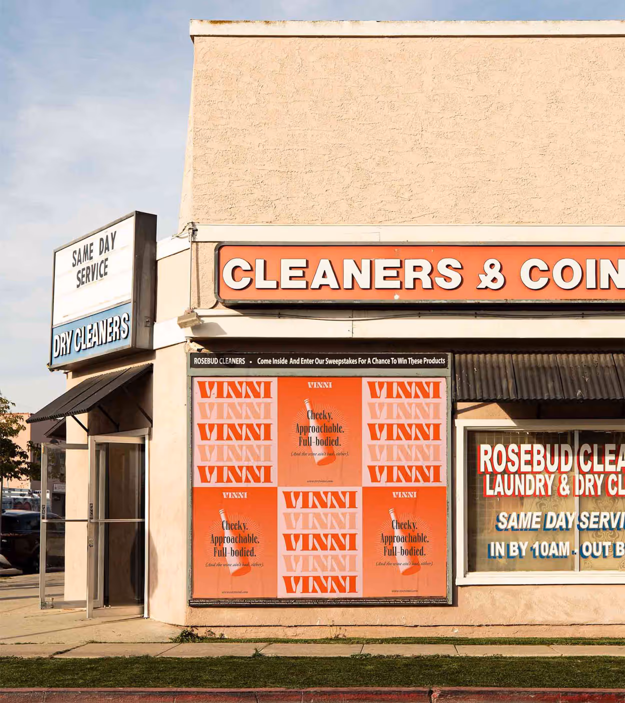 Exterior of a dry cleaners with signage for same day service and a large colorful Vinni advertisement on the front wall.