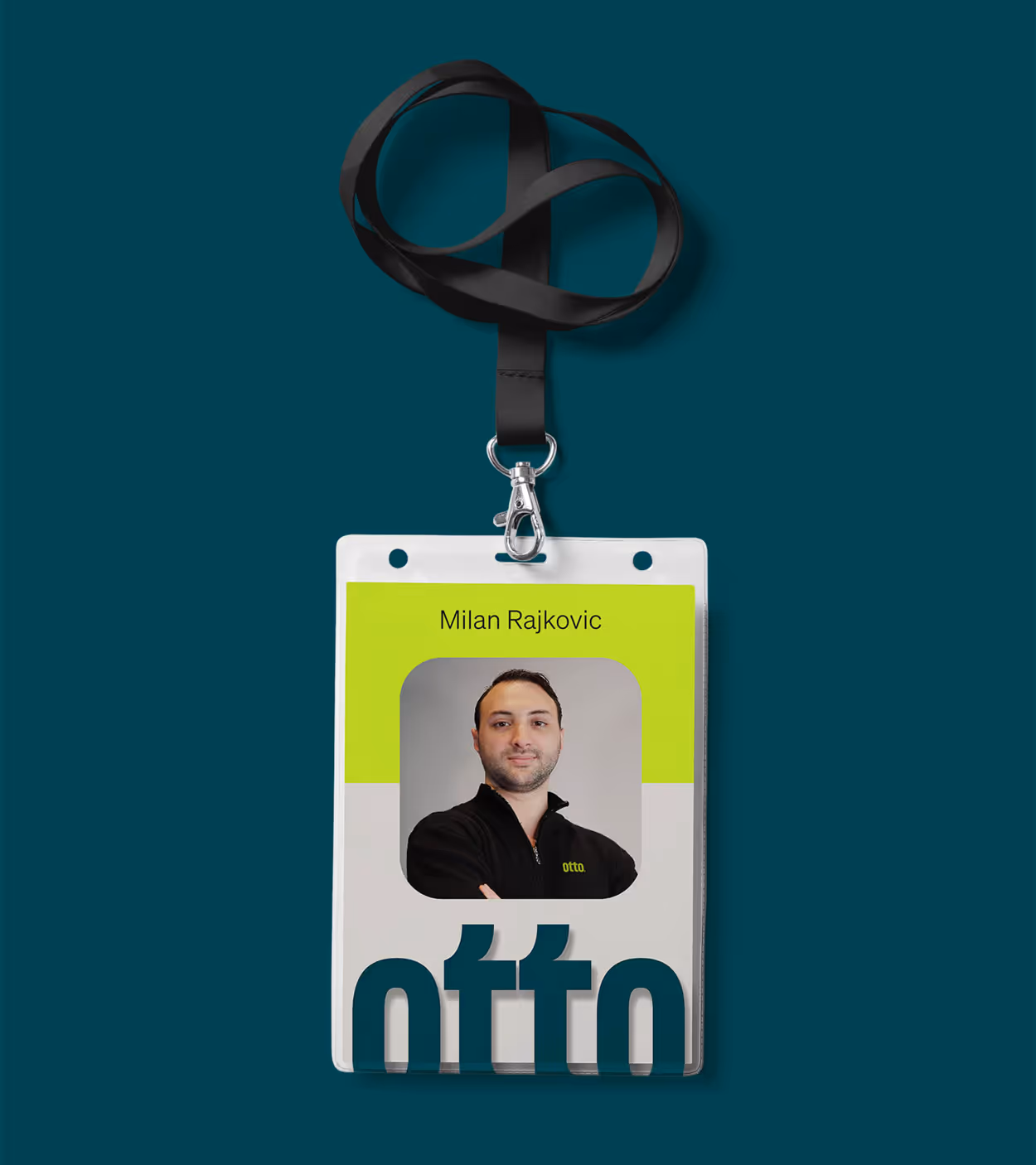 Employee ID badge with photo of a man named Milan Rajkovic wearing a black otto jacket, on a teal background with a black lanyard.