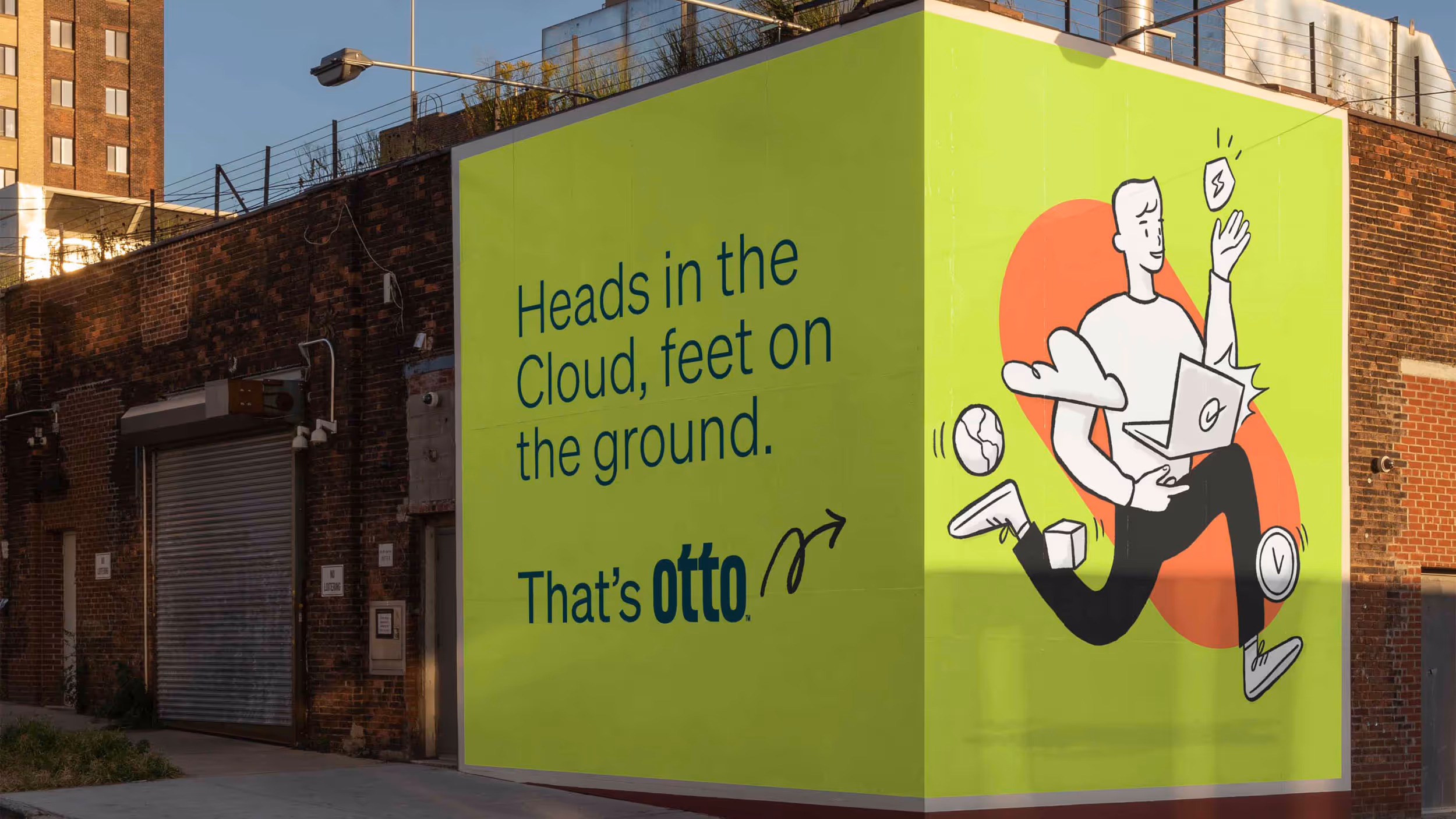 Street mural on a brick building corner with text 'Heads in the Cloud, feet on the ground. That’s otto' and illustration of a person running with a laptop and floating icons.