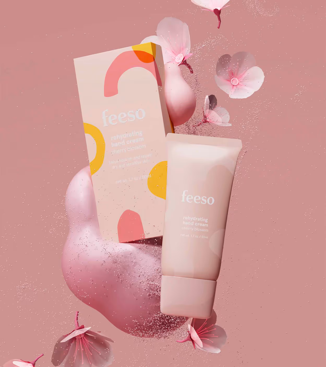 FeeSo rehydrating cherry blossom hand cream tube and packaging surrounded by pink cherry blossom petals on a pink background.