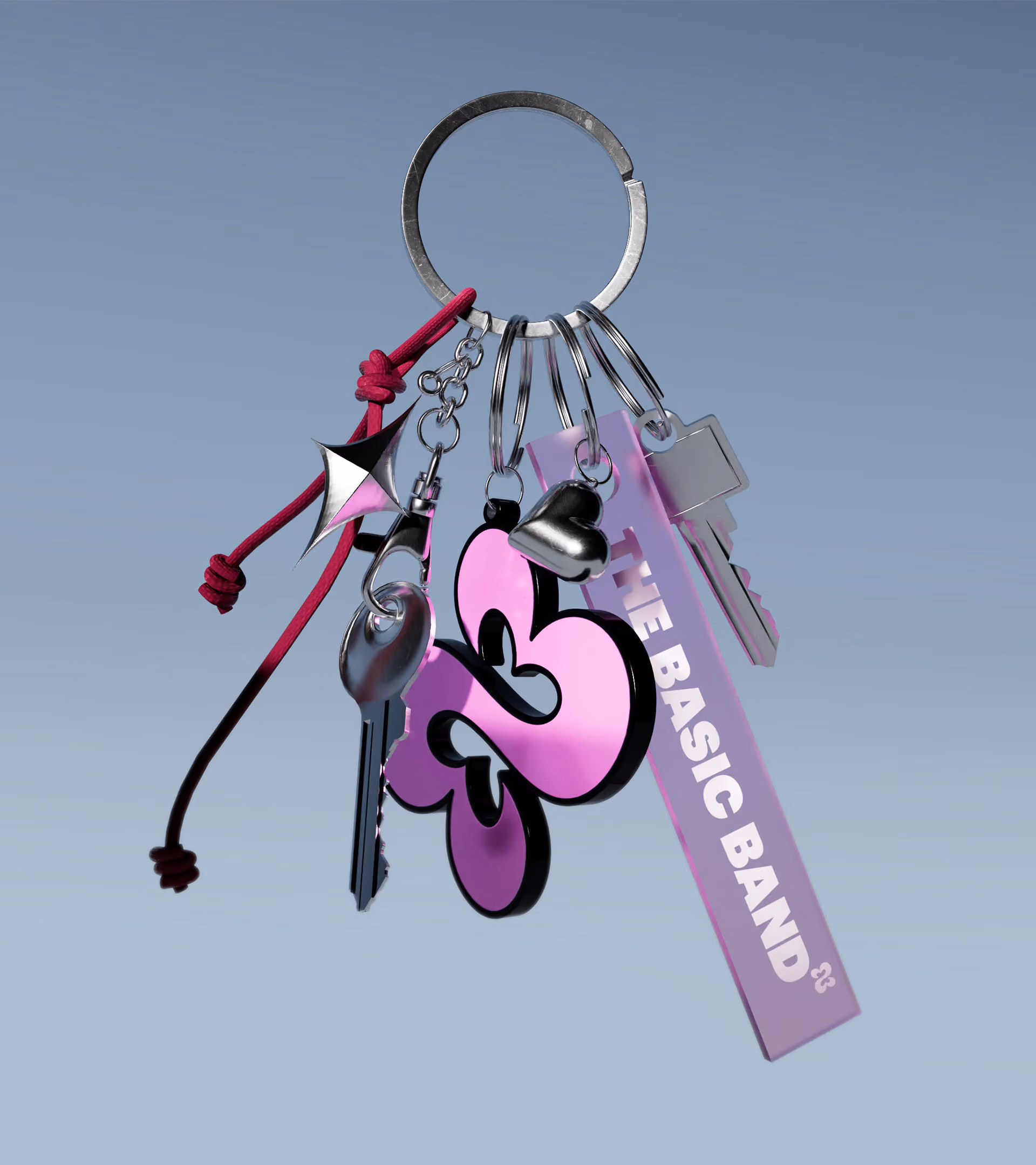 Metal keyring holding two silver keys, a pink and black butterfly-shaped charm, a silver heart pendant, a pink tag that reads 'THE BASIC BAND', and a red knotted cord with a geometric charm.