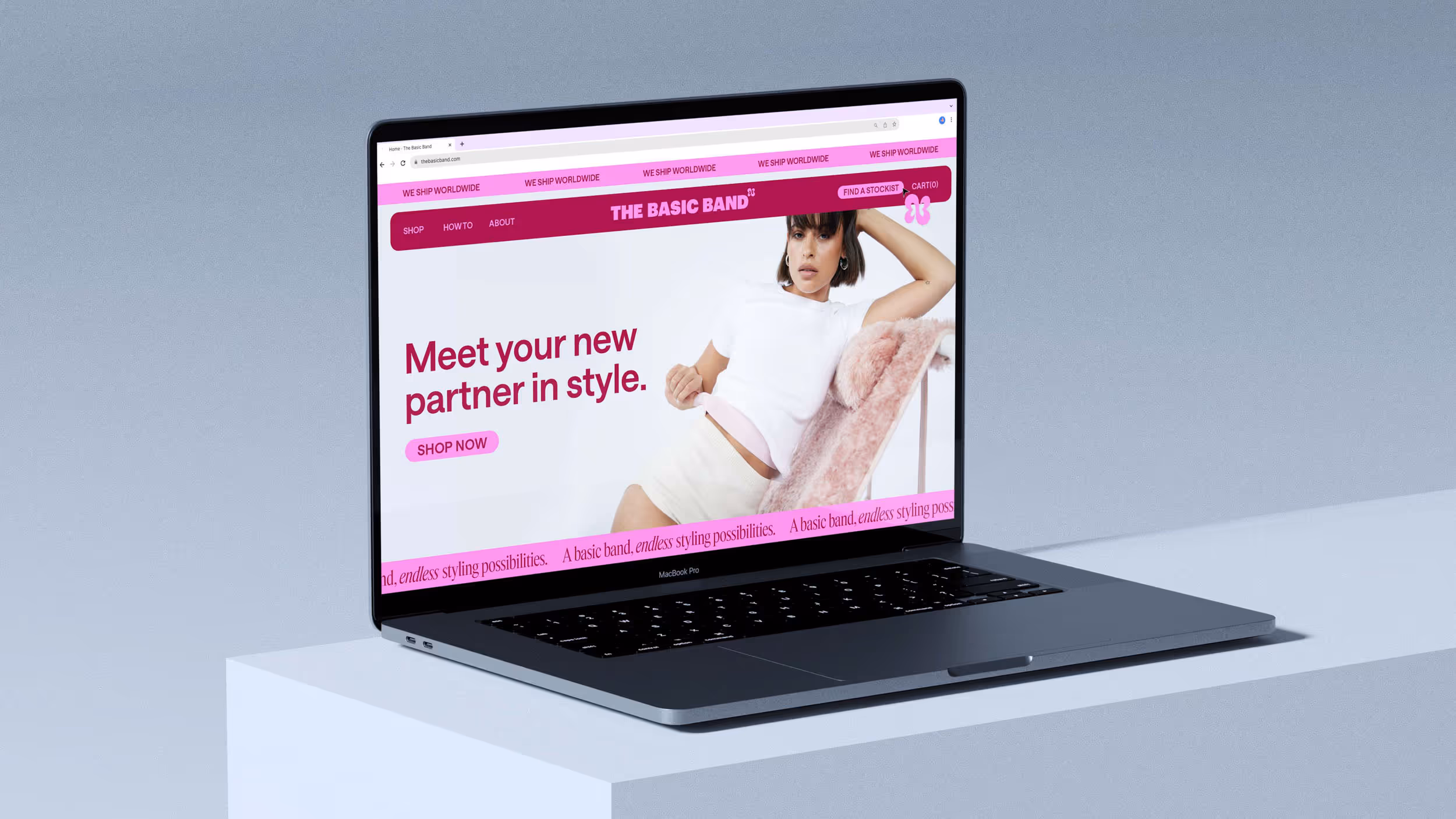 MacBook Pro laptop displaying The Basic Band website with a woman reclining on a chair and text saying 'Meet your new partner in style.'