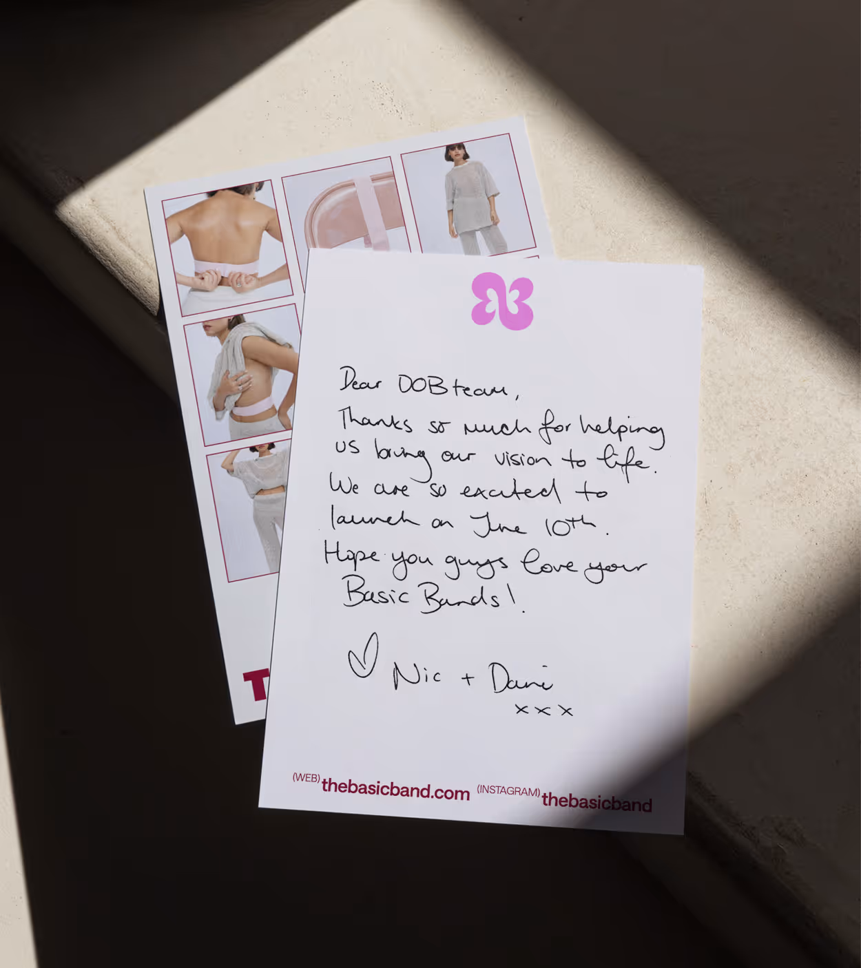 Handwritten thank you note from Nic and Dani to DOB team, expressing excitement for launch on June 10th, placed on a surface with a small product flyer featuring models wearing clothing.
