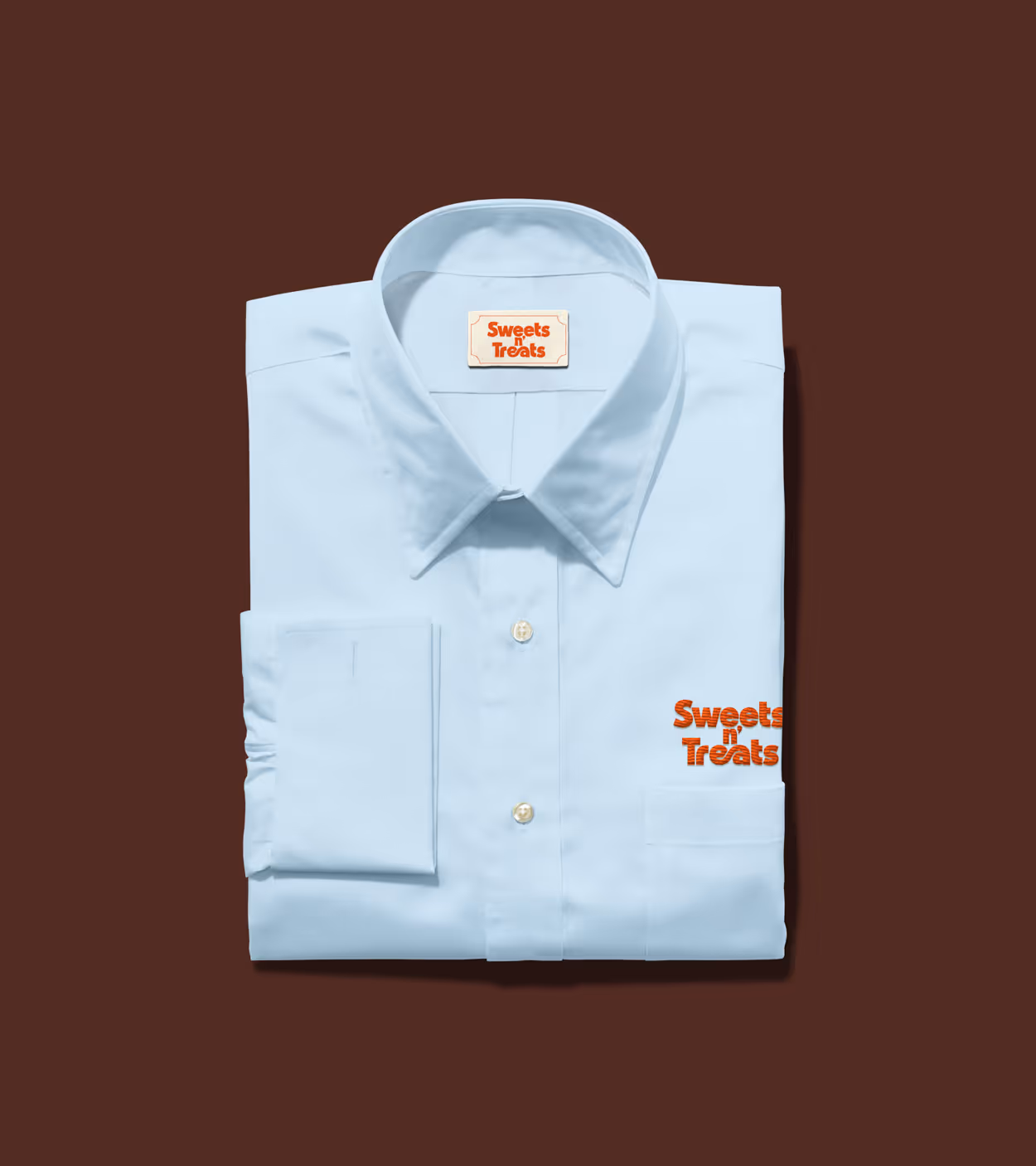 Light blue folded dress shirt with Sweets n' Treats logo embroidered in orange on the pocket and printed on the collar label.