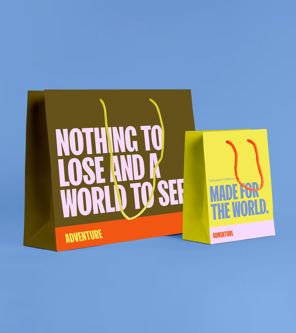 Two colorful paper shopping bags on a blue background, one large olive green bag with yellow handles and text 'NOTHING TO LOSE AND A WORLD TO SEEE' with 'ADVENTURE' in orange, next to a smaller bright yellow bag with red handles and text 'MADE FOR THE WORLD' and 'ADVENTURE' in orange.