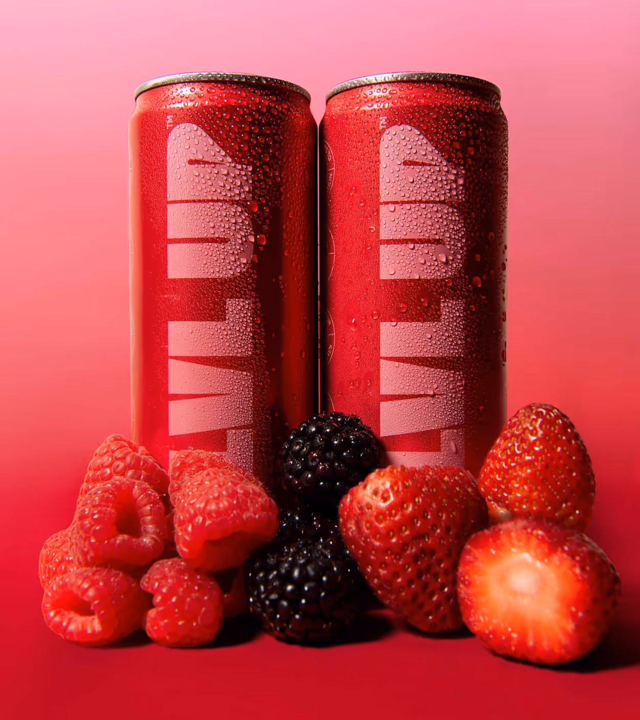 Two red energy drink cans with water droplets surrounded by raspberries, blackberries, and strawberries on a red gradient background.