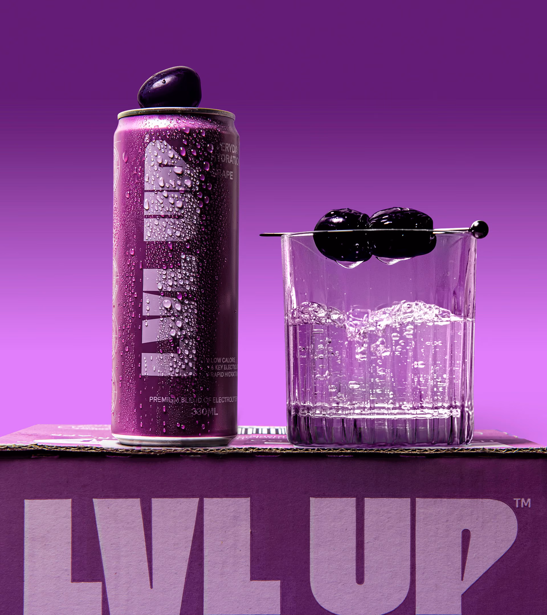 Purple can of LVL UP electrolyte drink with water droplets, grape on top, next to a glass of bubbly water garnished with two dark grapes on a skewer.