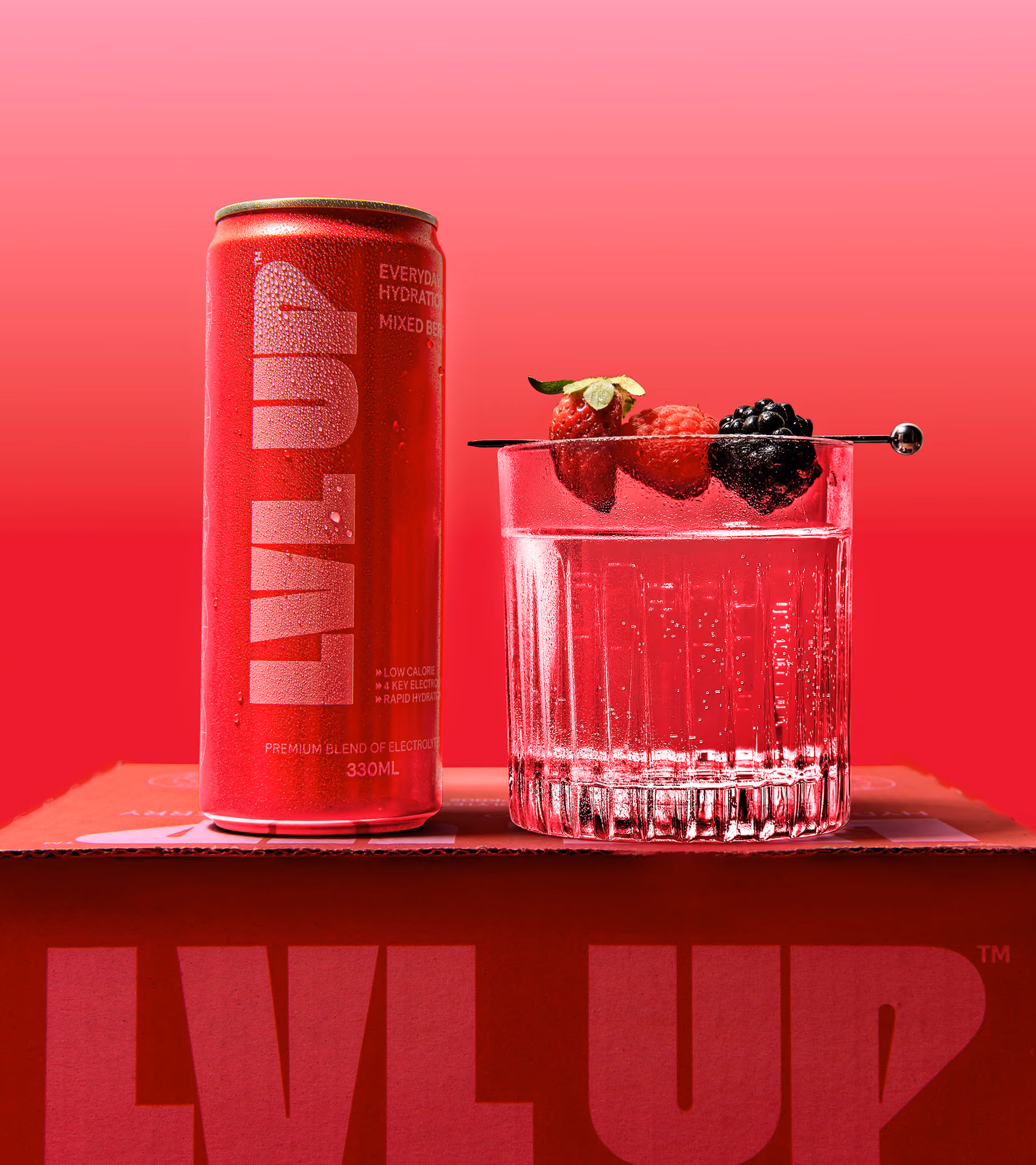 Red LVL UP drink can next to a glass of sparkling water garnished with strawberry, raspberry, and blackberry on a matching red box.
